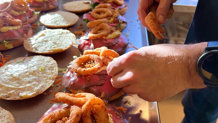 En r&aelig;kke roastbeefsandwiches er ved at blive tilberedt. Et par h&aelig;nder er ved at l&aelig;gge l&oslash;gringe &oslash;verst p&aring; sandwichen.